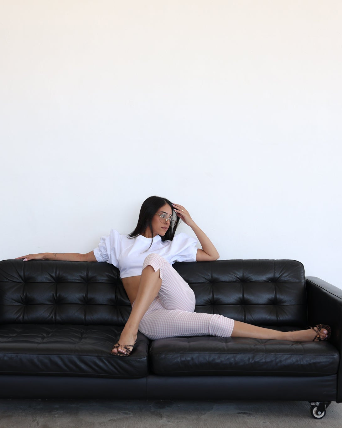 A woman reclining on a black leather tufted sofa against a plain white wall.