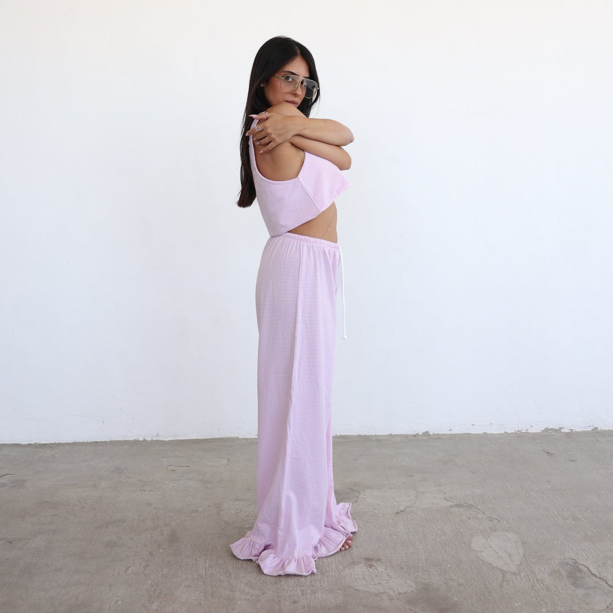 A woman modeling a light pink two-piece outfit consisting of a sleeveless crop top and a matching long skirt, standing against a plain white wall and concrete floor.