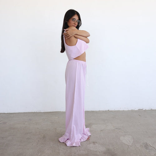 A woman modeling a light pink two-piece outfit consisting of a sleeveless crop top and a matching long skirt, standing against a plain white wall and concrete floor.